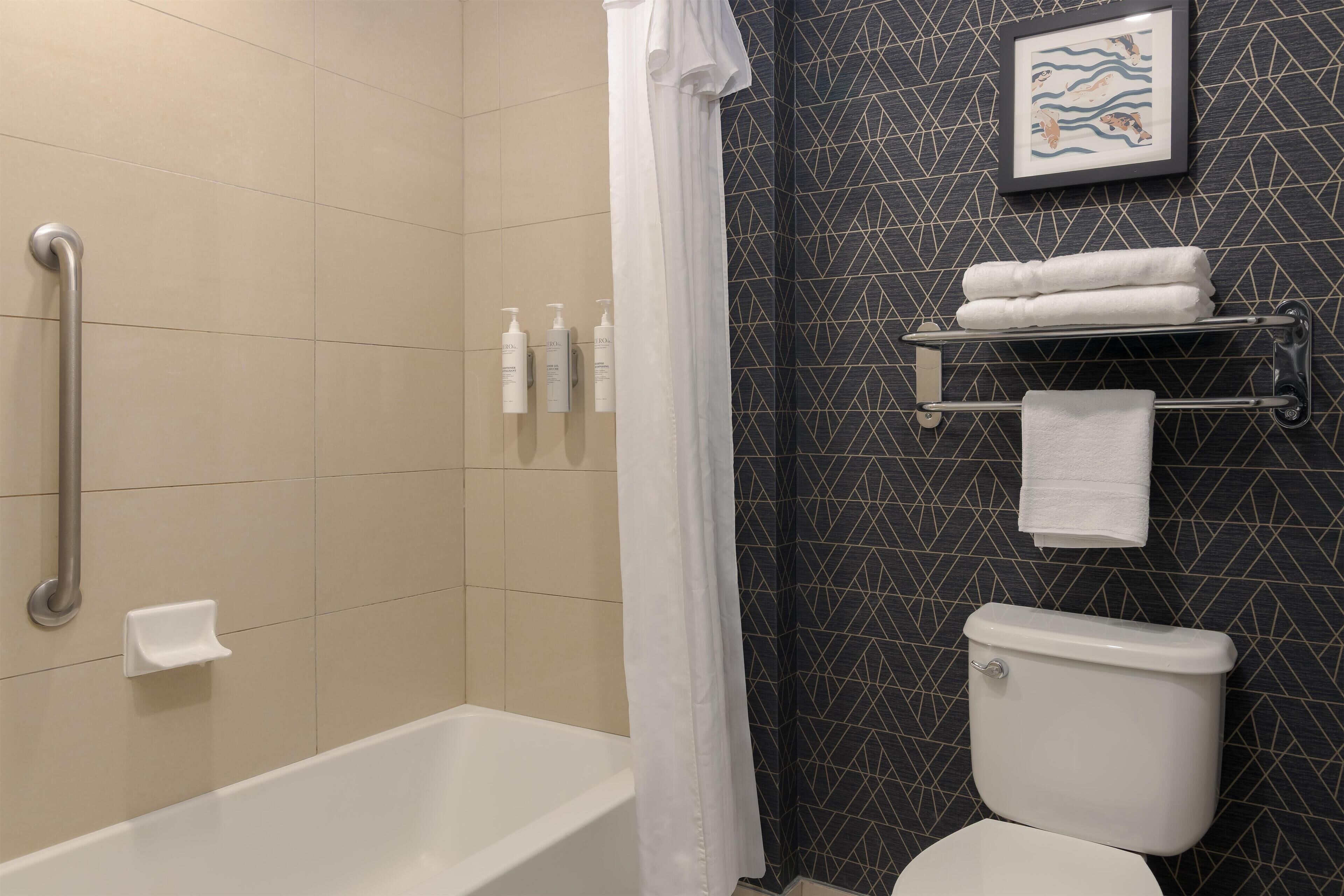 Et badeværelse med badekar, toilet, bruseforhæng og et håndklædestativ.