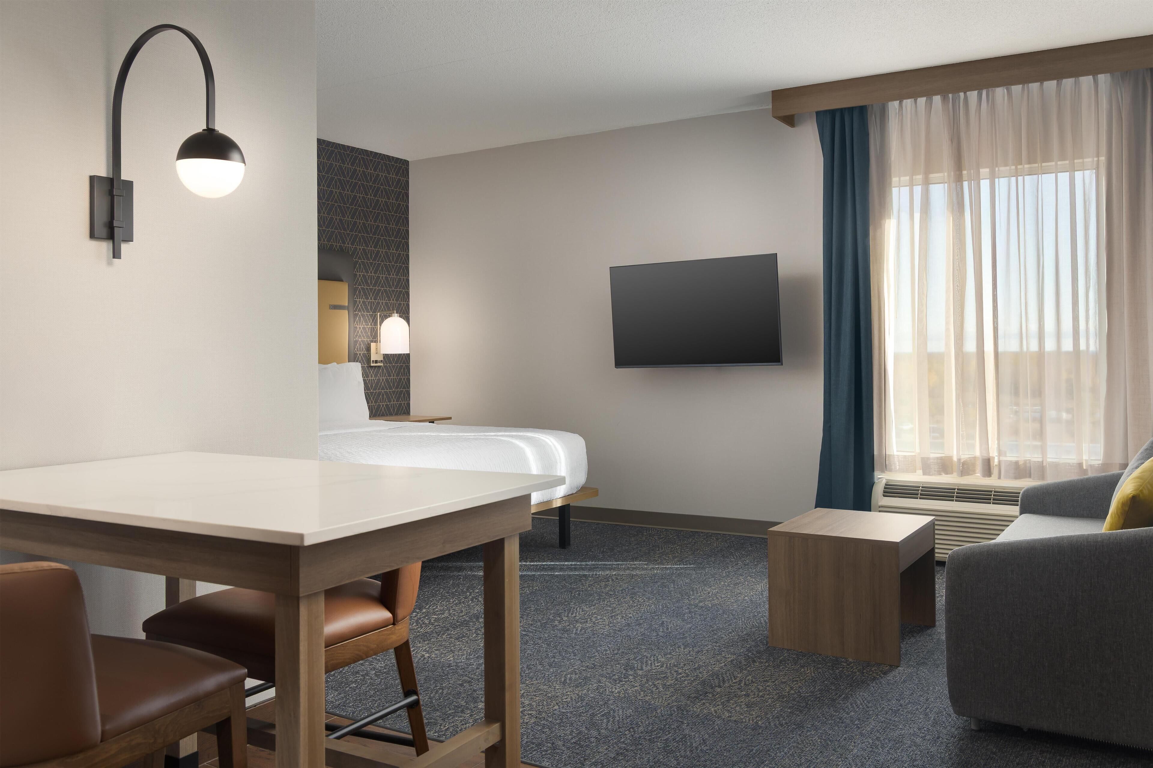 A hotel room with a bed, a desk, a chair, a sofa, a TV, and a window with curtains.