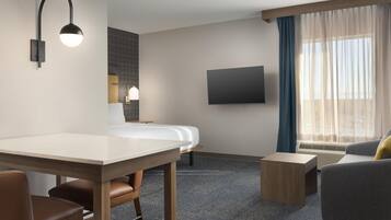 A hotel room with a bed, a desk, a chair, a sofa, a TV, and a window with curtains.