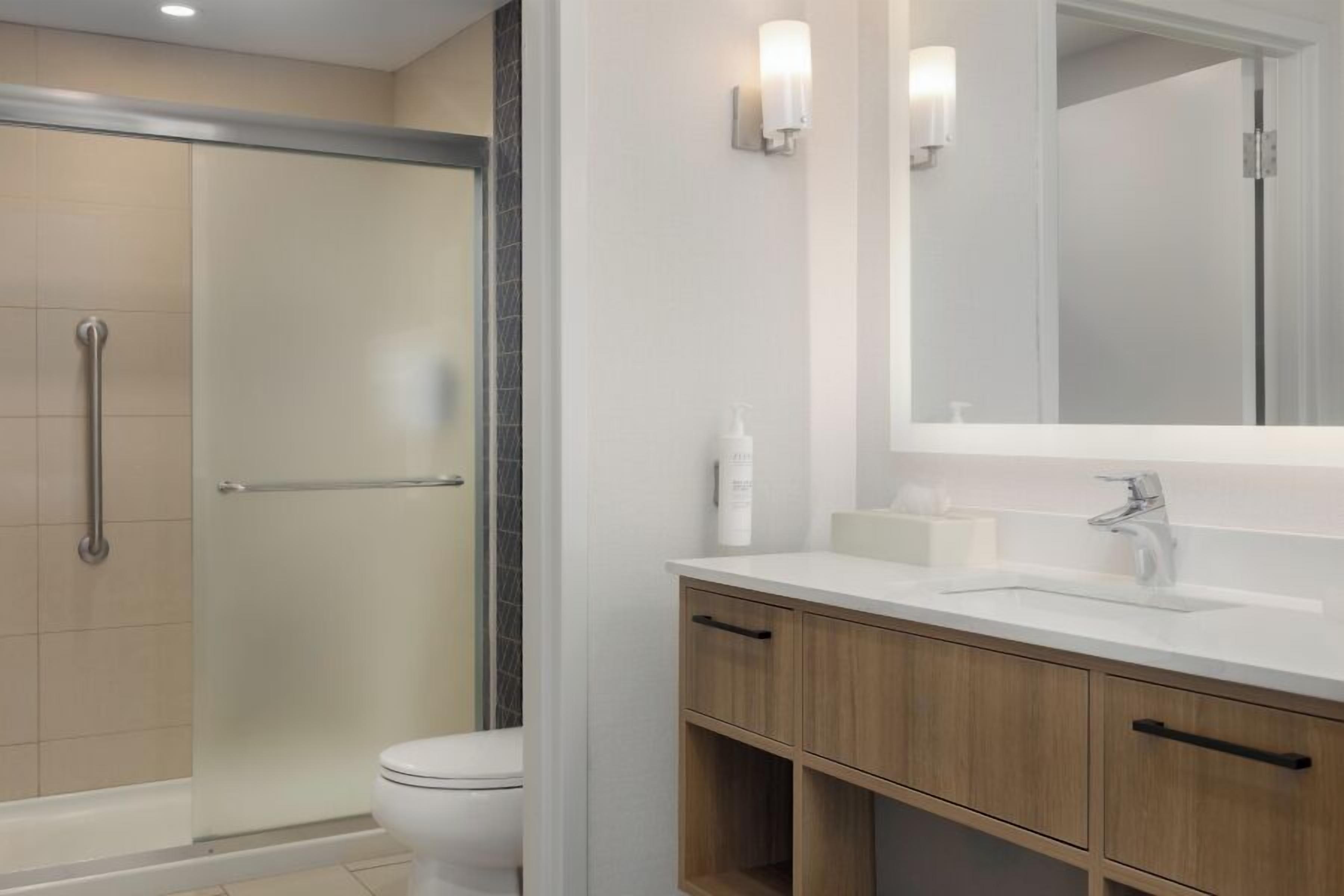 A modern bathroom with a glass shower enclosure, a white toilet, a sink with a mirror, and wooden cabinets.