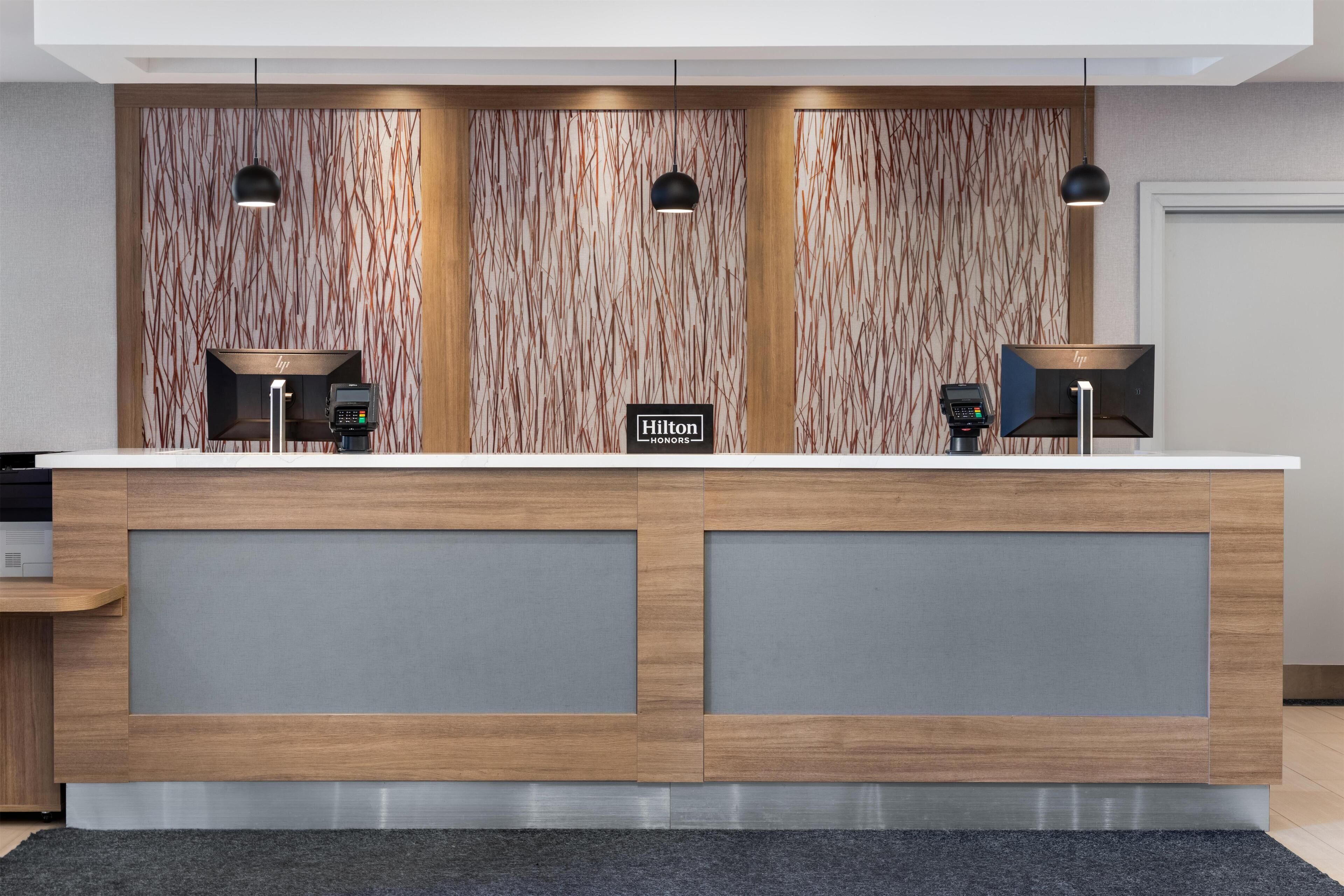 A modern hotel reception desk with two counters, each with a digital kiosk and a sign indicating 'Hilton Honors'.