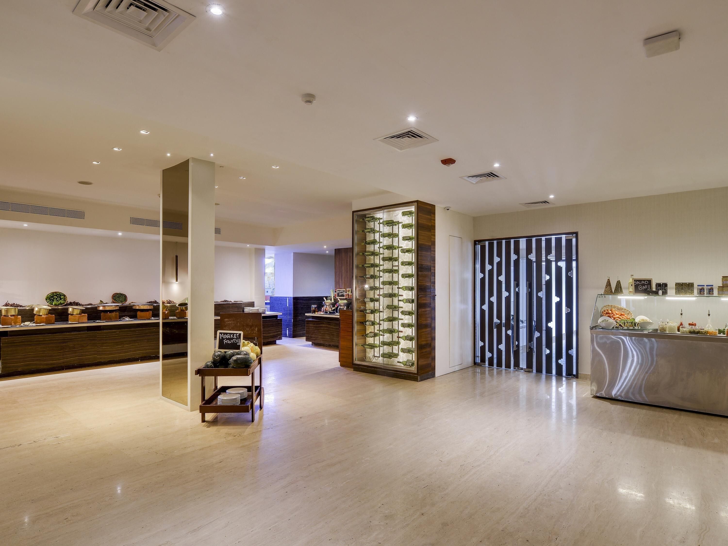 Un hall d’hôtel moderne avec une colonne centrale, un comptoir d’accueil et un espace buffet.