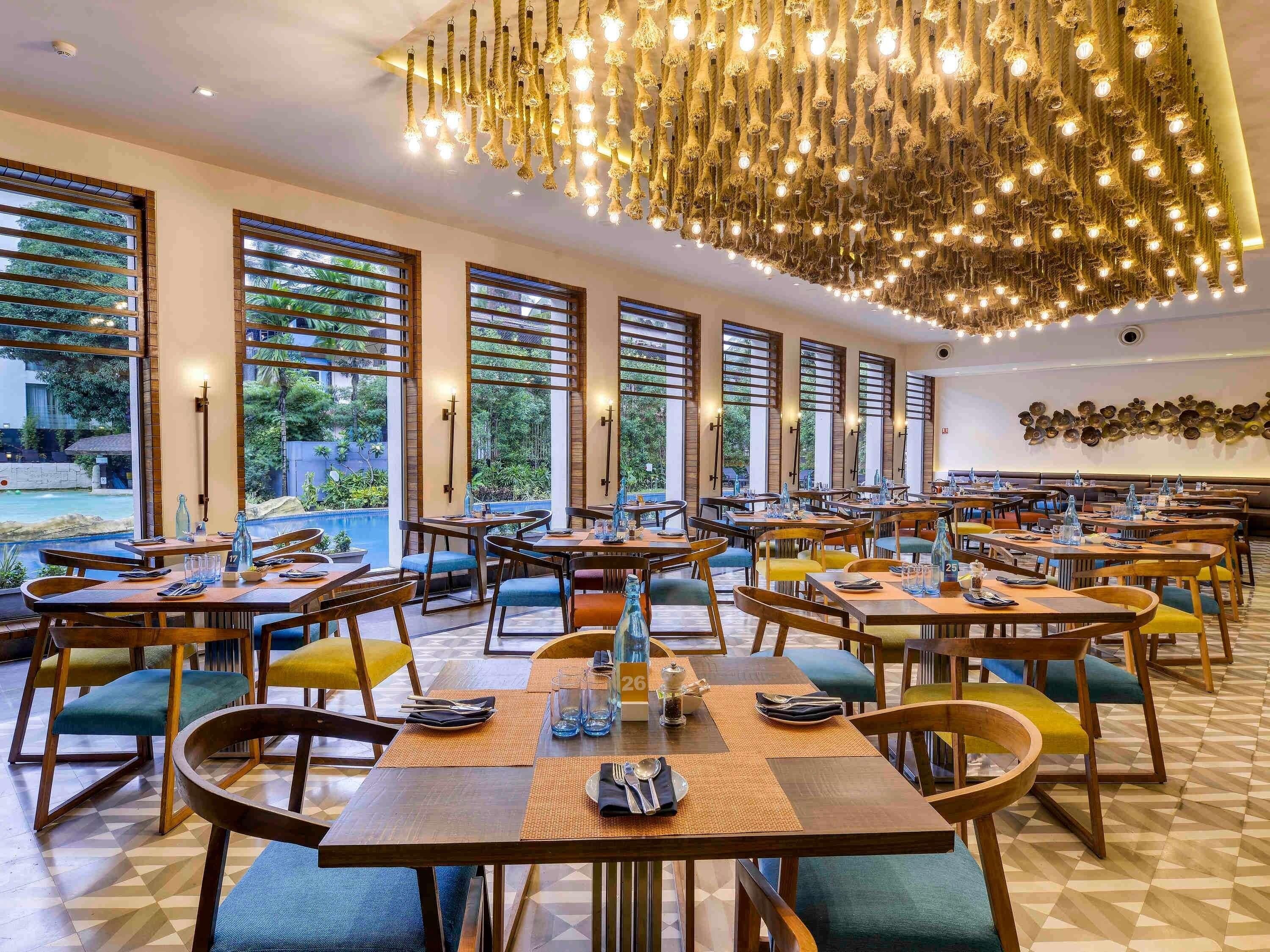 A restaurant with multiple tables and chairs, large windows, and a hanging light fixture.