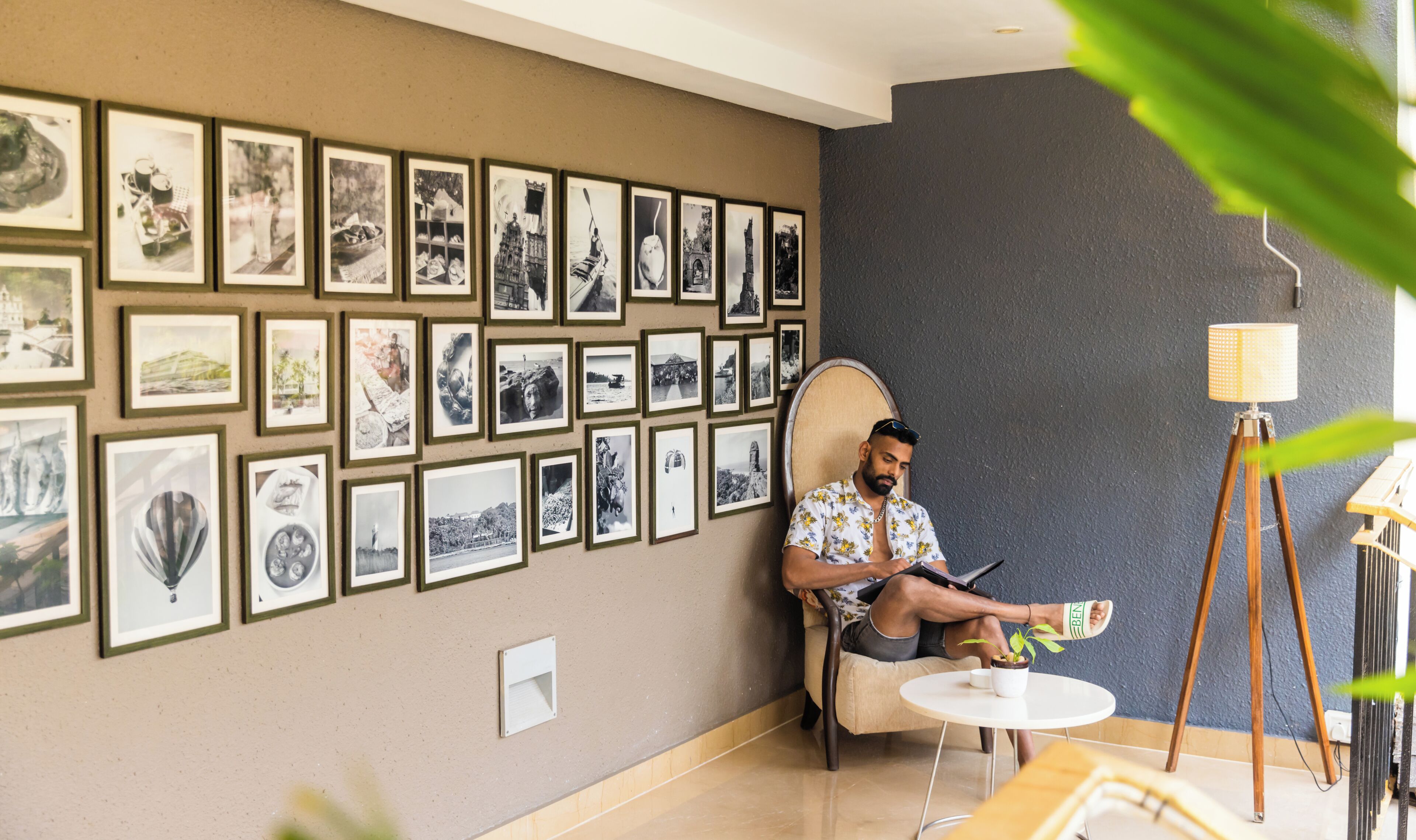 Una habitación con una pared de fotografías enmarcadas, una mesa redonda con una planta y una lámpara de pie.