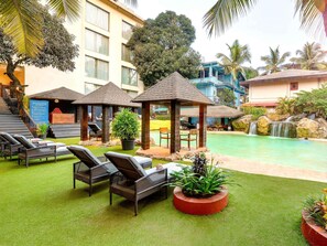 A poolside area with lounge chairs, a small waterfall, and a building in the background. - Novotel Goa Candolim Hotel (Candolim)