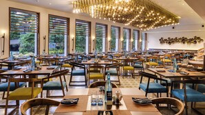 A spacious restaurant with multiple tables and chairs, large windows, and a modern chandelier. - Novotel Goa Candolim Hotel (Candolim)