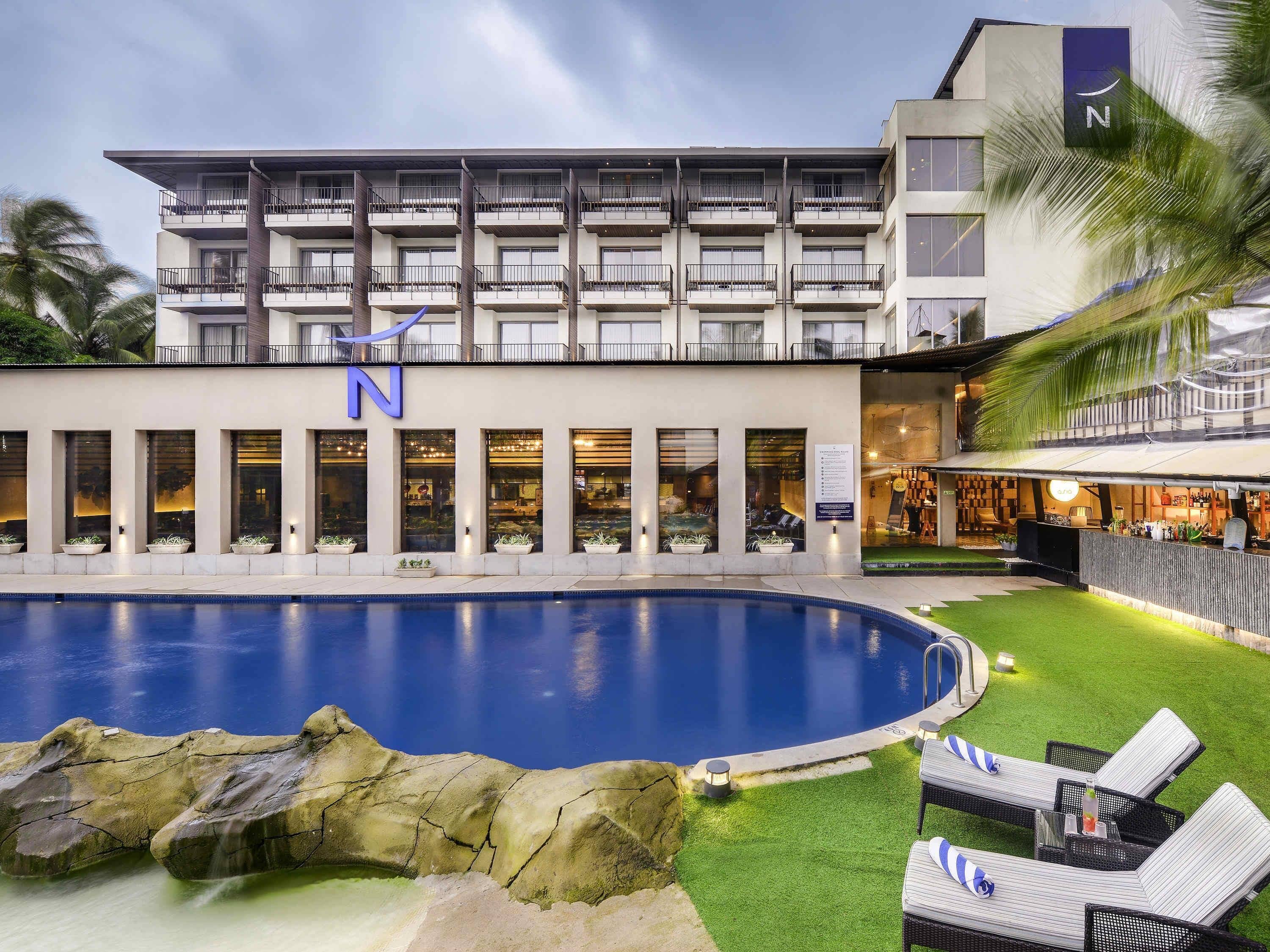 A hotel with a swimming pool, outdoor seating, and a well-lit facade.
