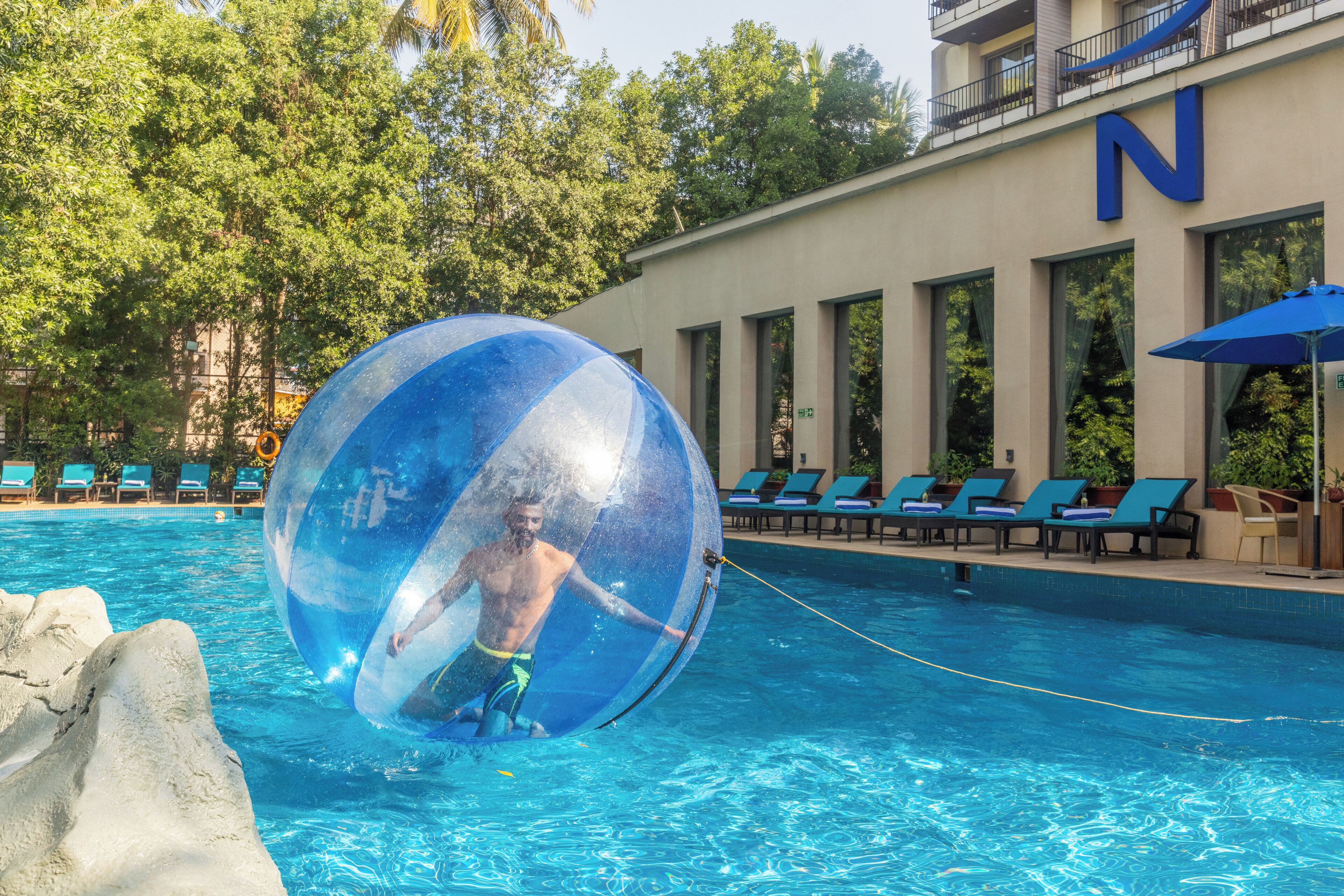 A swimming pool with a large transparent ball, lounge chairs, and a building with a 'N' sign.