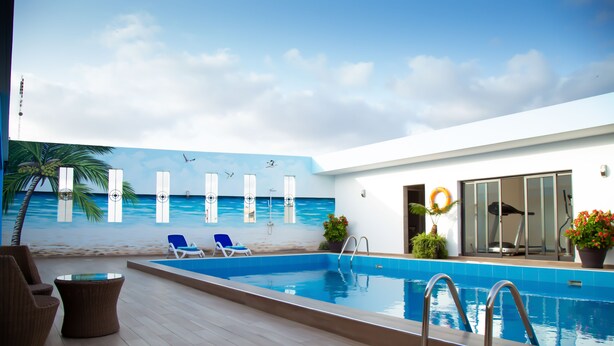 Una piscina interior con un mural al estilo playa, sillas de descanso y un gimnasio.