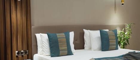 A hotel room with a bed, pillows, a bedside table with a phone, a wall-mounted light, and a potted plant.