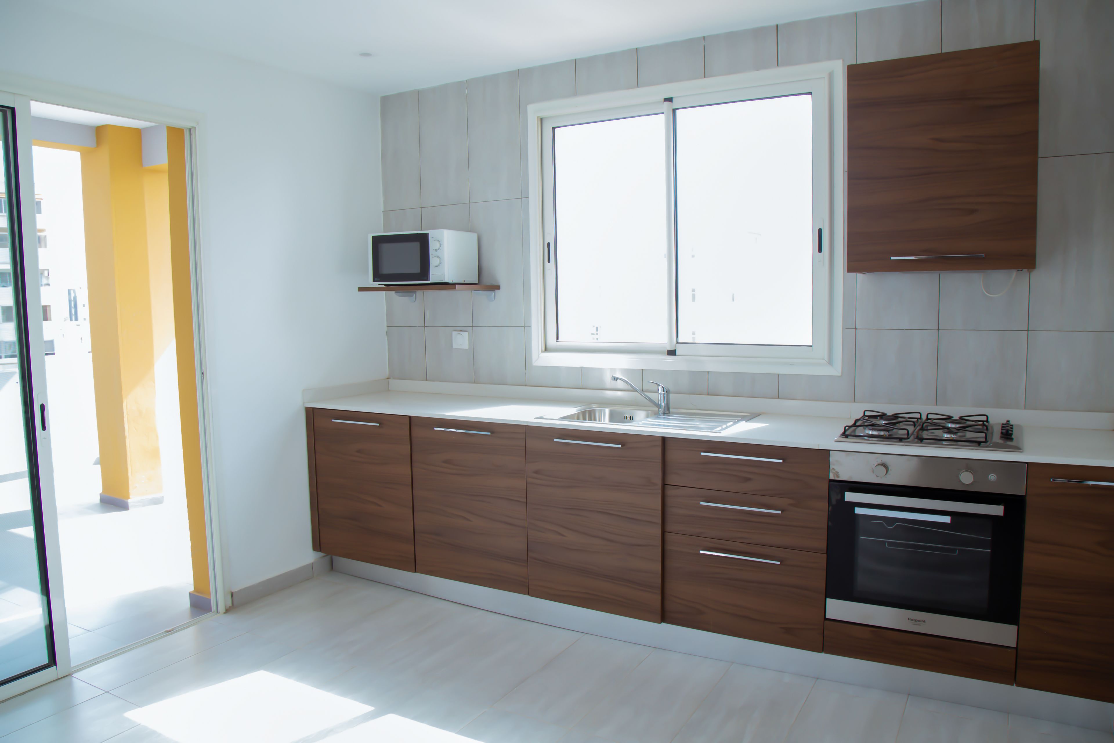 Una cocina moderna con armarios de madera, microondas integrado, pileta de acero inoxidable y cocina a gas.