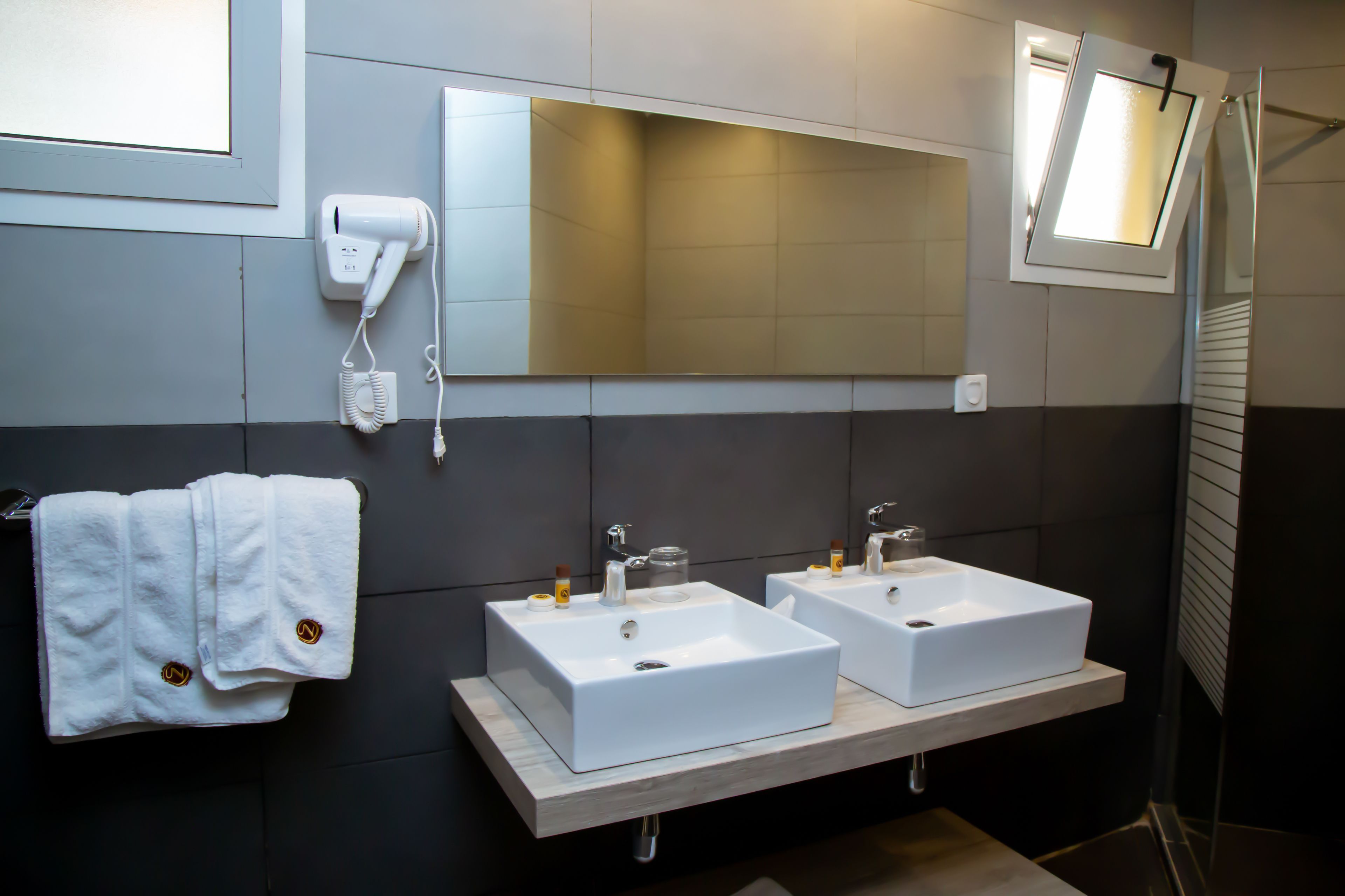 Un baño moderno con dos lavamanos blancos, un secador de pelo y un espejo.