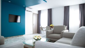 Una sala de estar moderna con una pared azul de acento, un televisor de pantalla plana, una mesa de centro de vidrio con flores y una zona de estar con un sofá y sillones.