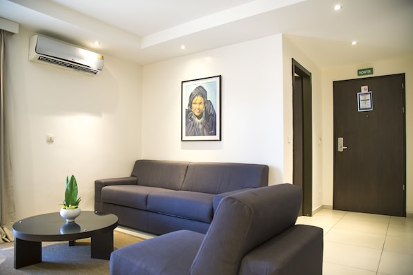 A modern living room with a grey sofa, a round coffee table, and a framed picture on the wall. - Le Ndiambour Hôtel et Résidence (Dakar)