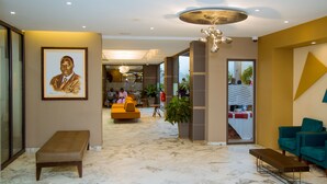 Un vestíbulo moderno con suelo de mármol, un retrato grande enmarco y una zona de estar con un sofá amarillo y un sillón verde azulado.