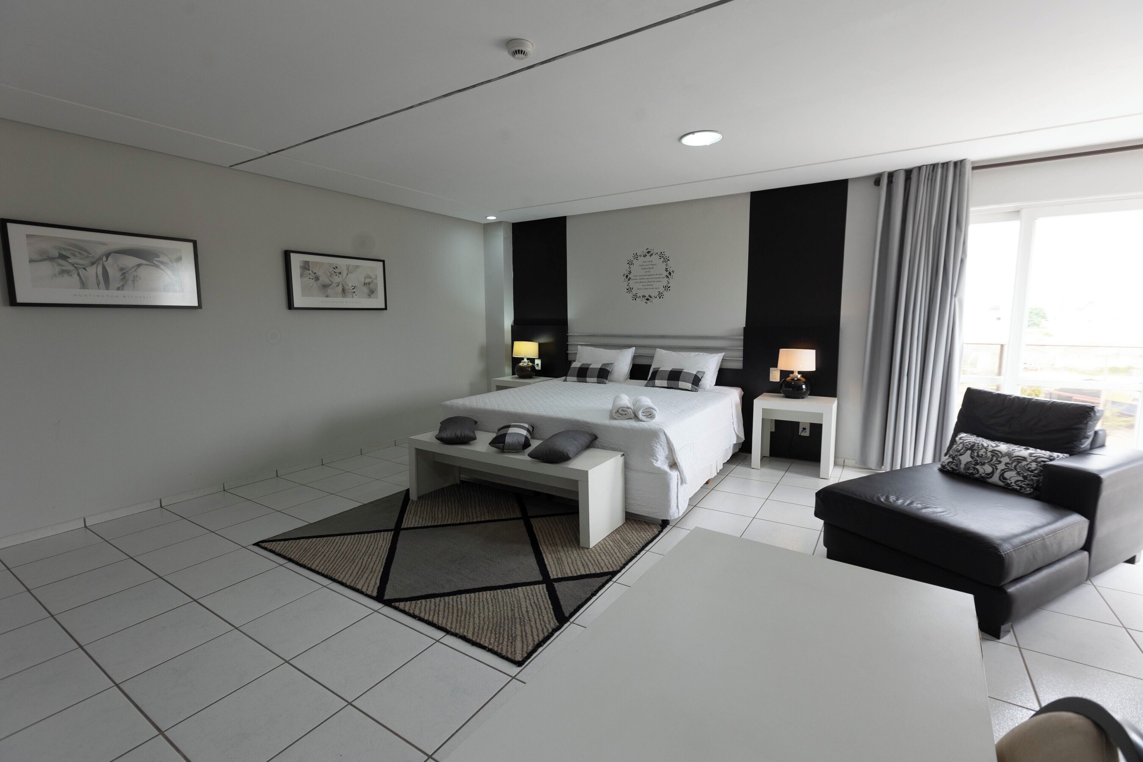 A modern hotel room with a large bed, a sofa, a desk, and two bedside tables.