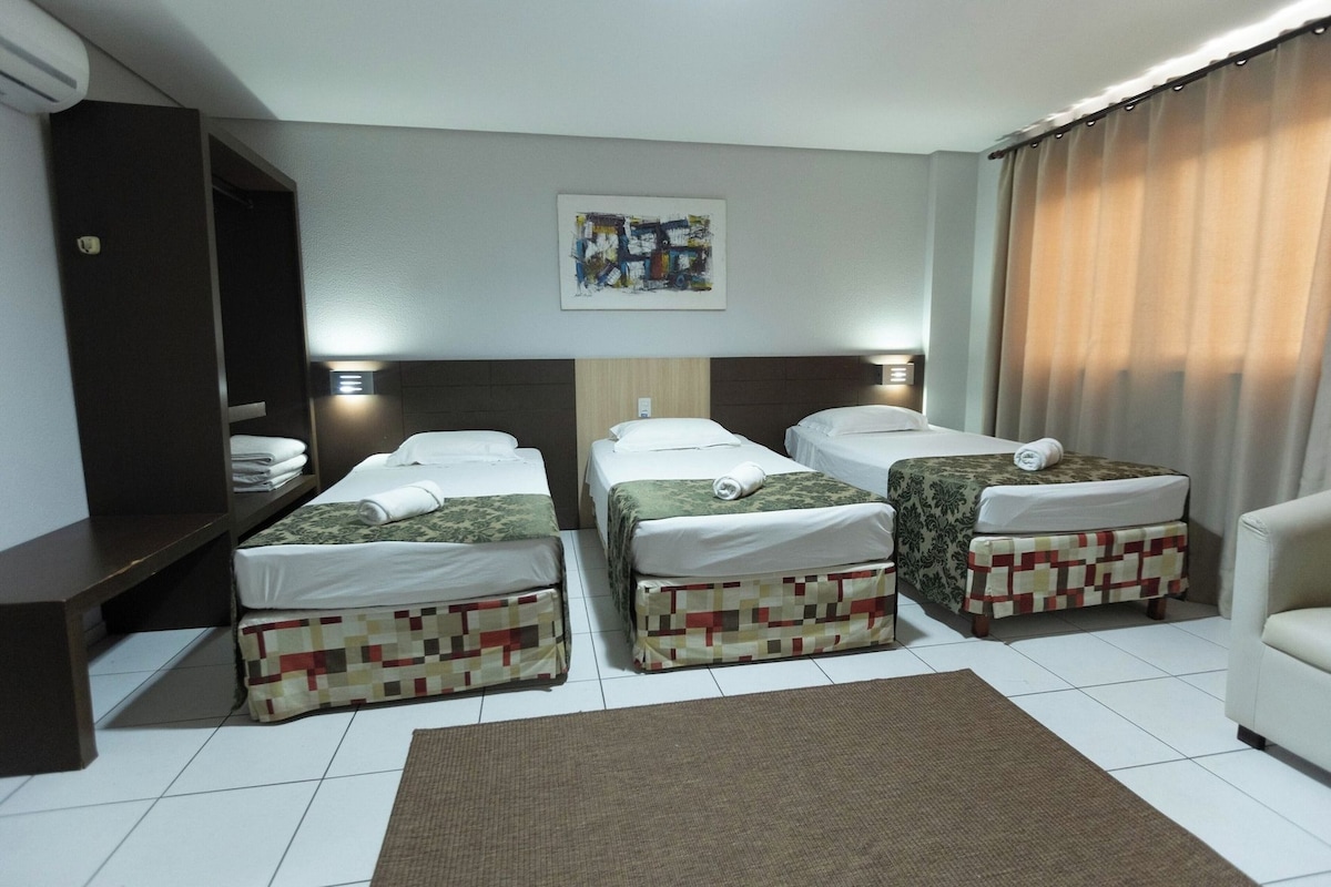 Habitación de hotel con tres camas, un sofá, un cuadro en la pared y una cortina.