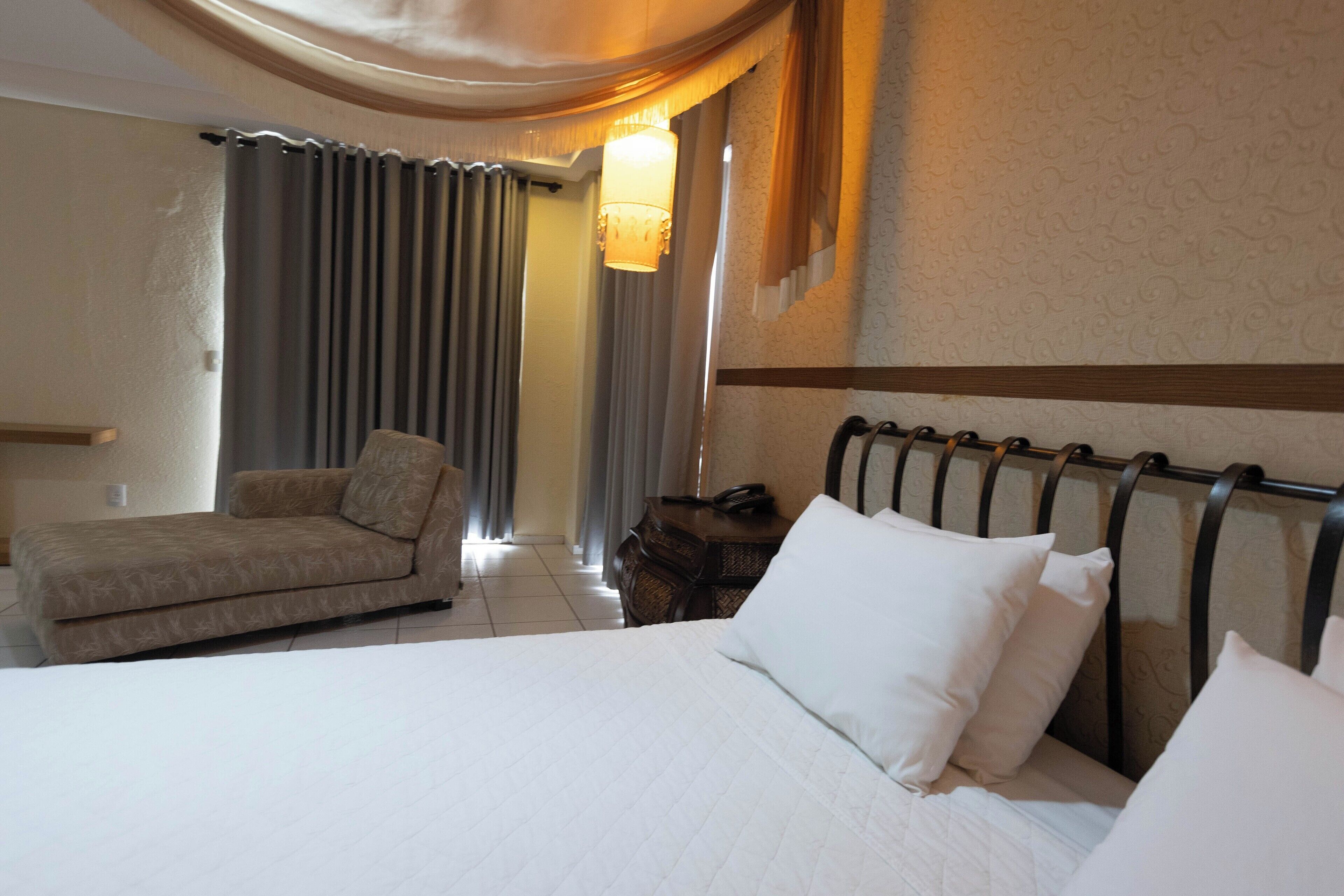 Una habitación de hotel con cama, una silla, una mesita de noche y una lámpara.