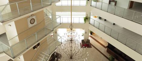 A multi-level atrium with glass railings, a central chandelier, and a geometric floor design.