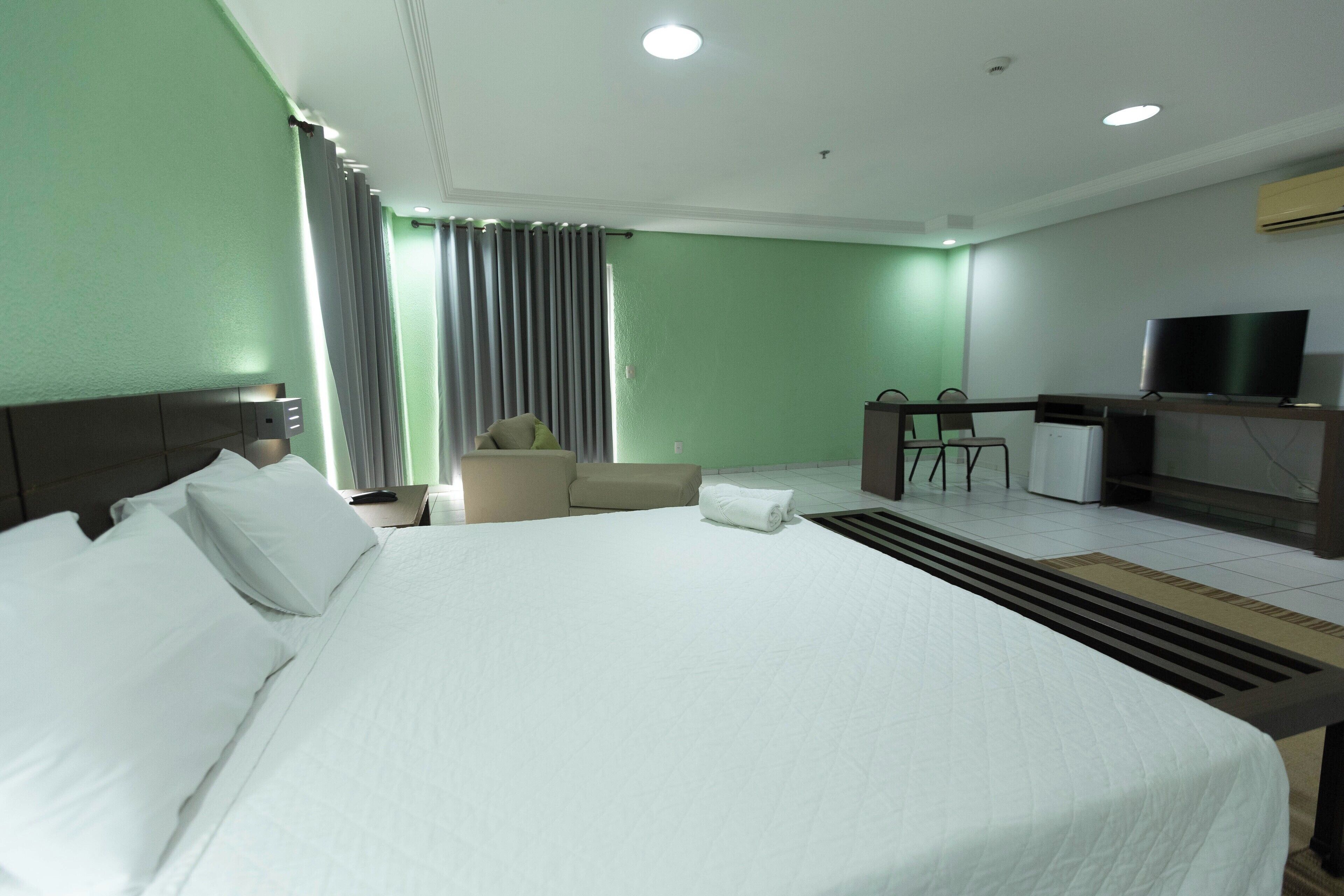 Una camera d'albergo con un letto grande, una scrivania con televisore, una sedia e un divano.