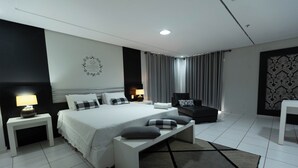 A modern hotel room with a large bed, bedside tables, a bench, a chair, and a patterned wall. - HITS PANTANAL HOTEL AEROPORTO (Varzea Grande)