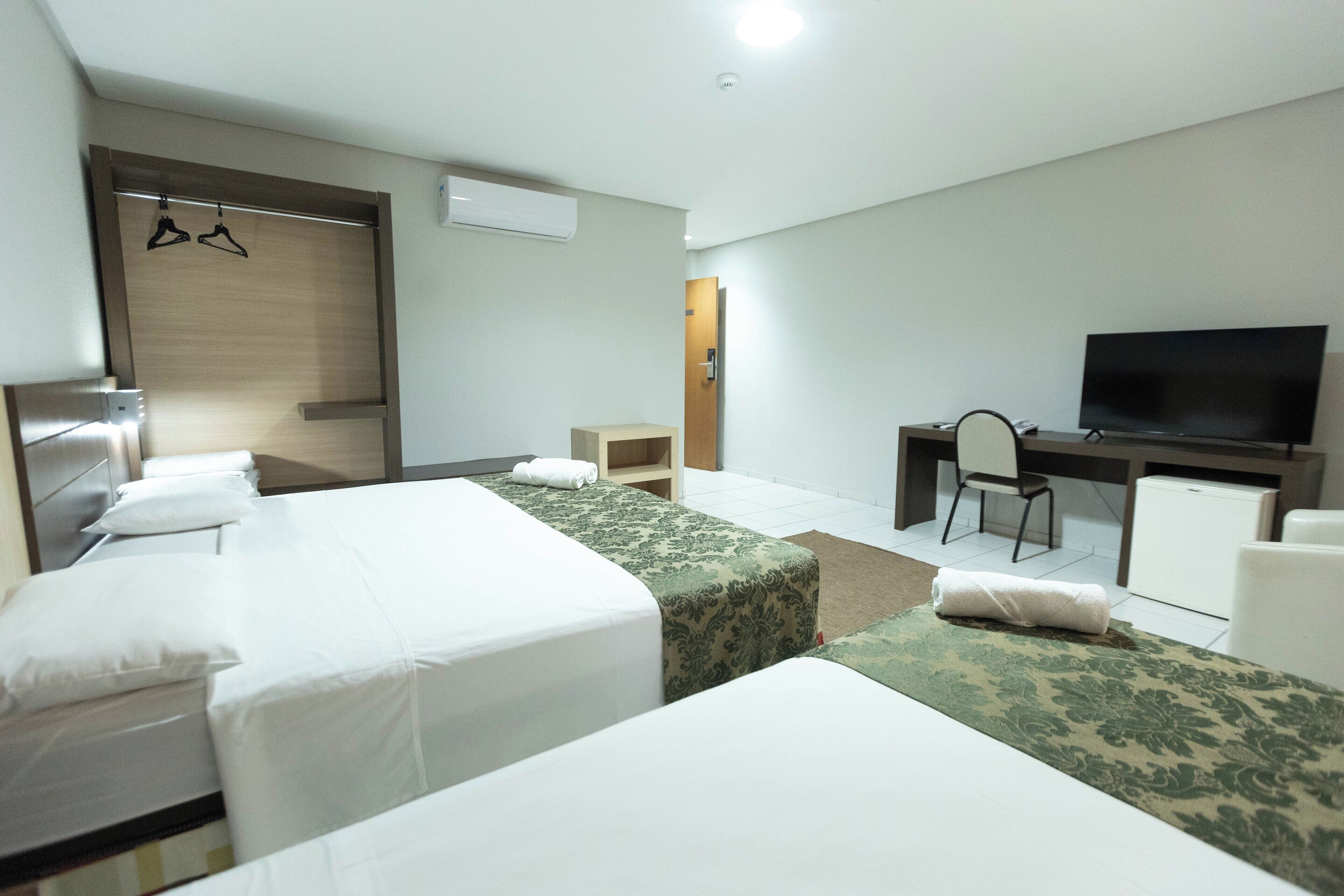 A hotel room with two beds, a desk, a chair, a TV, and a wardrobe.