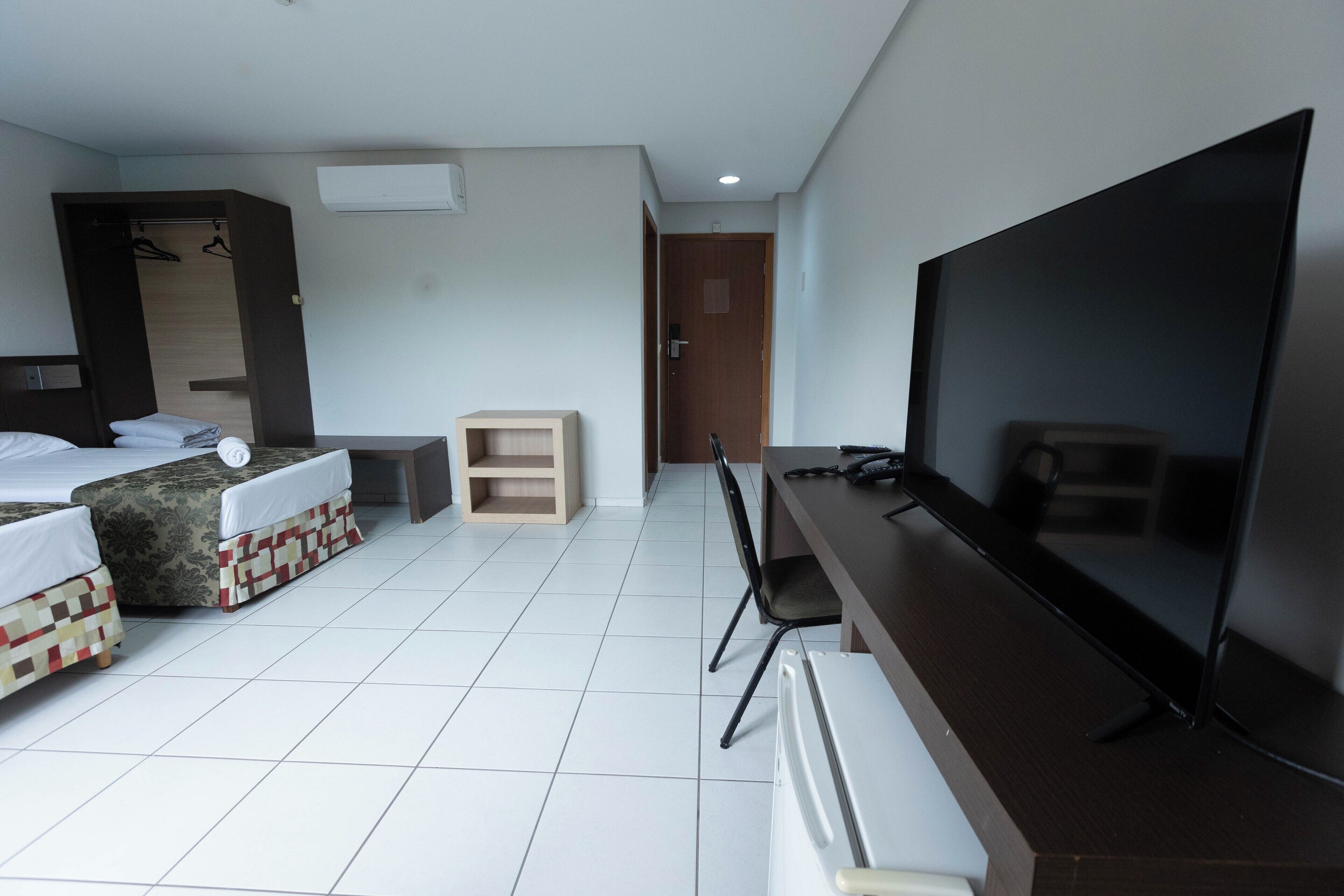 Une chambre d’hôtel comprenant un lit, un bureau avec une télévision, une chaise et une armoire.