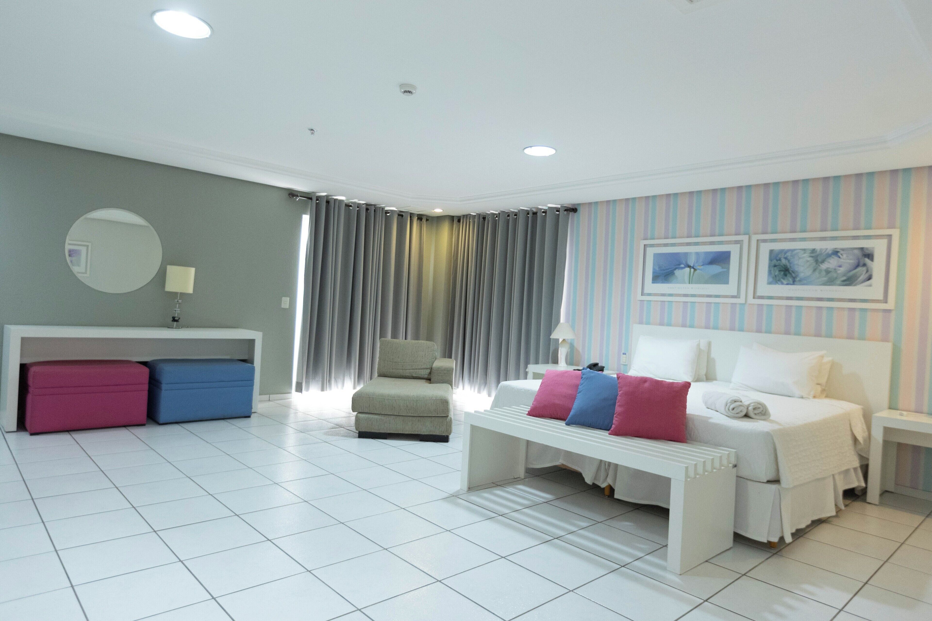Habitación de hotel moderna con una cama blanca, un banco, una silla y un escritorio con lámpara.