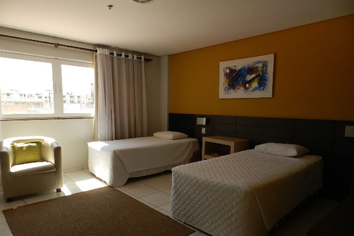 Habitación de hotel con dos camas, una silla, una mesita, un cuadro en la pared y vistas a la ciudad a través de la ventana.