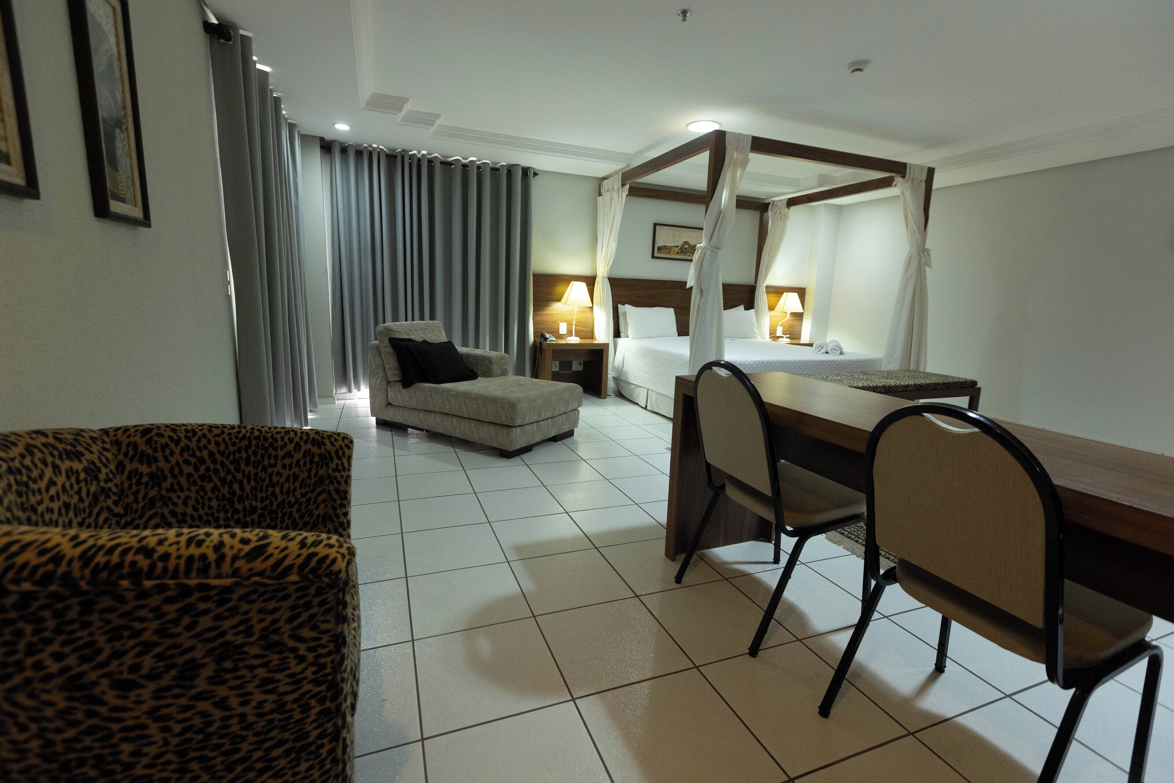 A hotel room with a bed, a desk, a chair, a sofa, and a nightstand with a lamp.