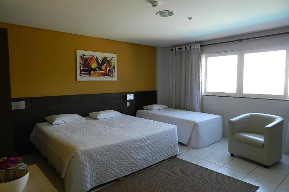 Habitación de hotel con dos camas, una silla, un cuadro en la pared y una ventana con cortinas.
