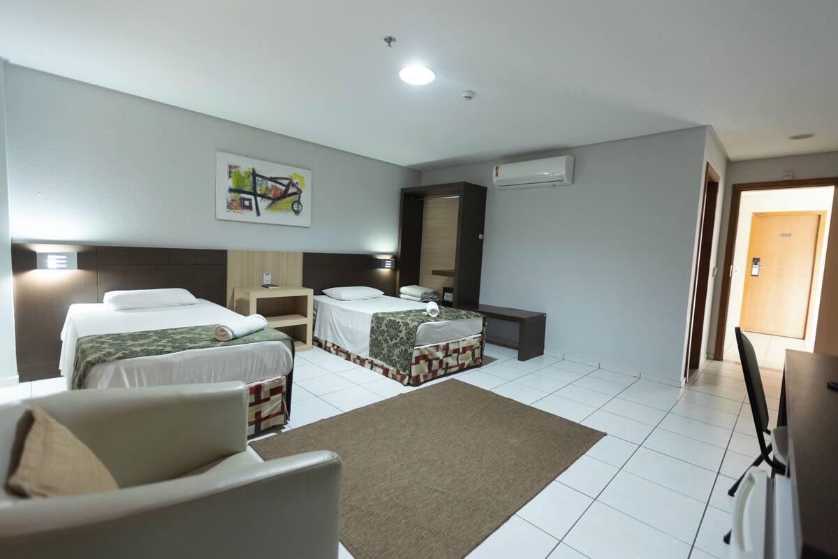 A hotel room with two beds, a desk, a chair, a sofa, and a large mirror.