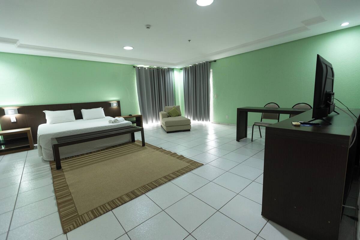 A hotel room with a bed, bedside tables, a desk, a chair, a television, and curtains.