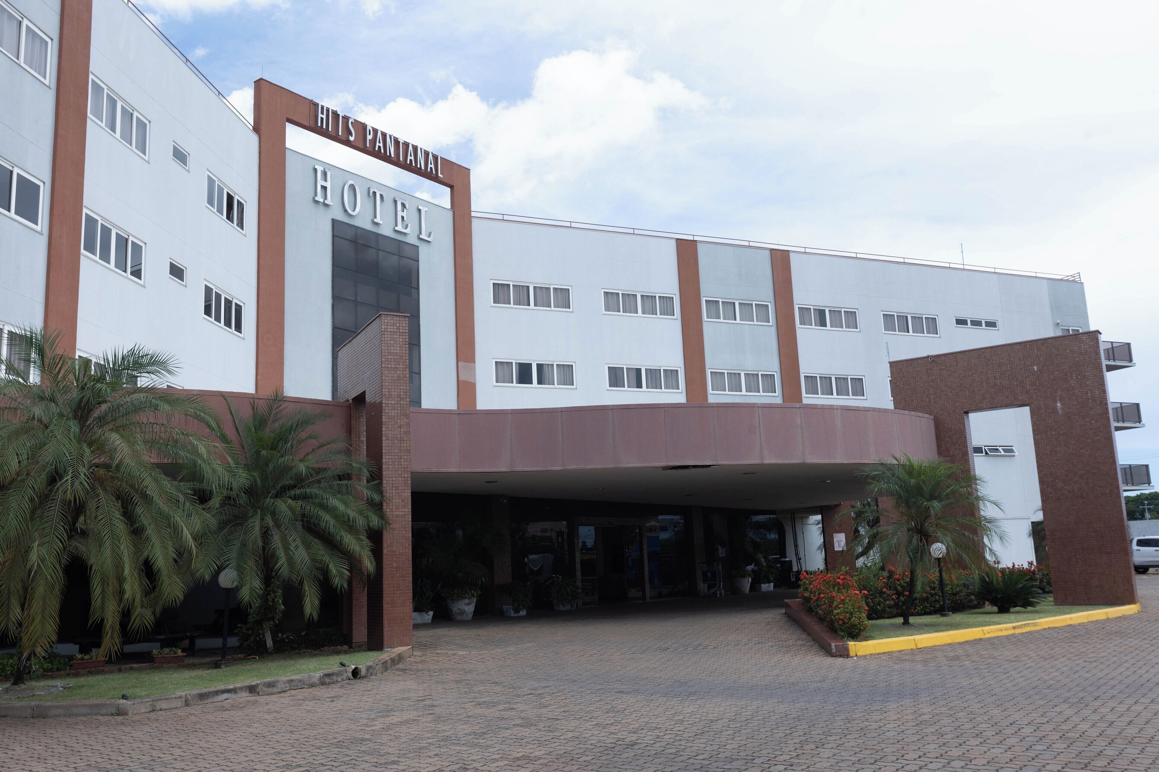 A modern hotel with a prominent entrance, multiple floors, and a well-maintained outdoor area with palm trees and potted plants.