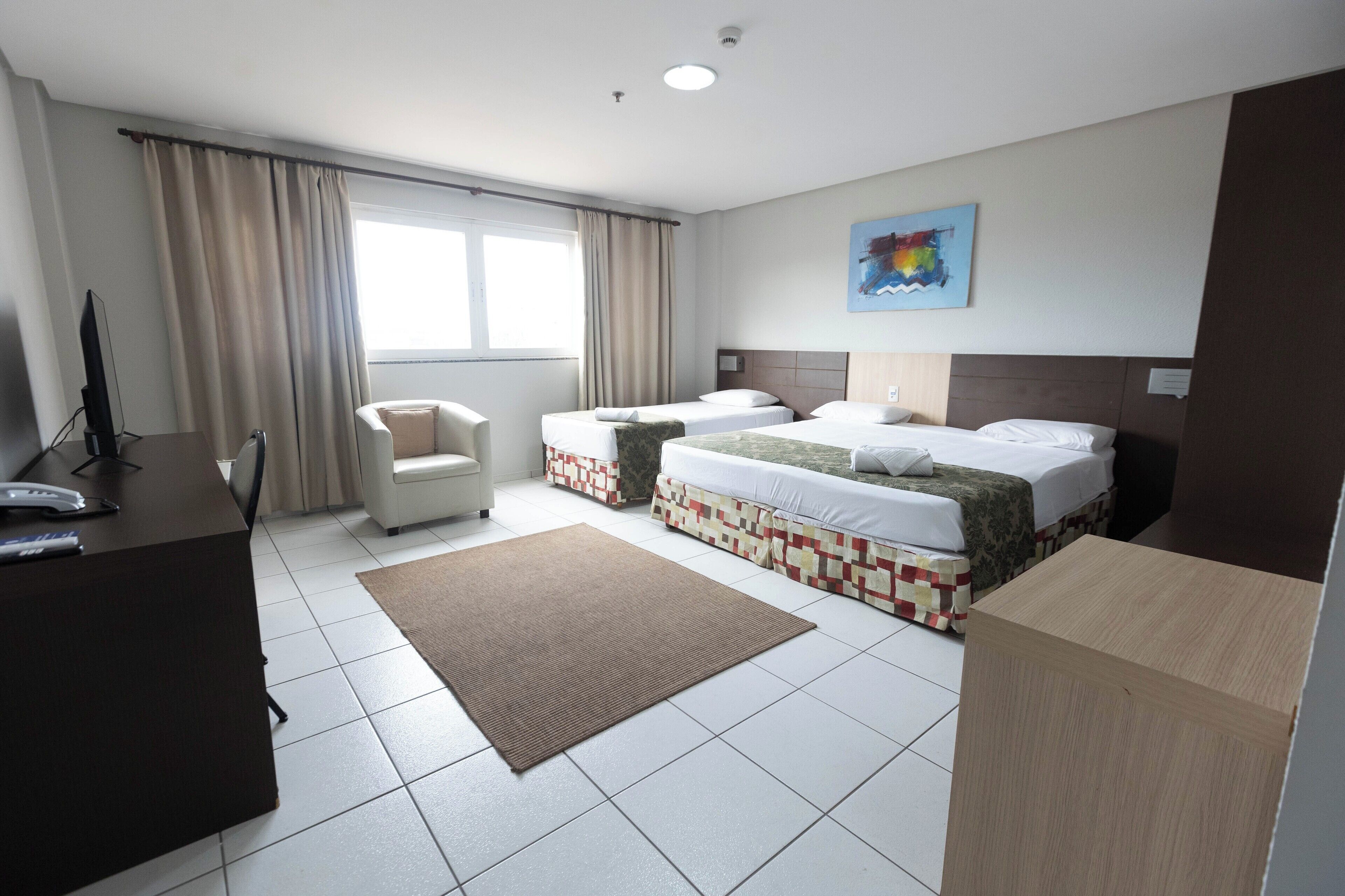 A hotel room with two beds, a desk, a chair, and a large window.