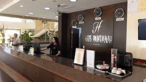A hotel reception desk with clocks displaying time in different cities, a sign reading "HITS PANTANAI HOTEL," and a coffee machine. - HITS PANTANAL HOTEL AEROPORTO (Varzea Grande)