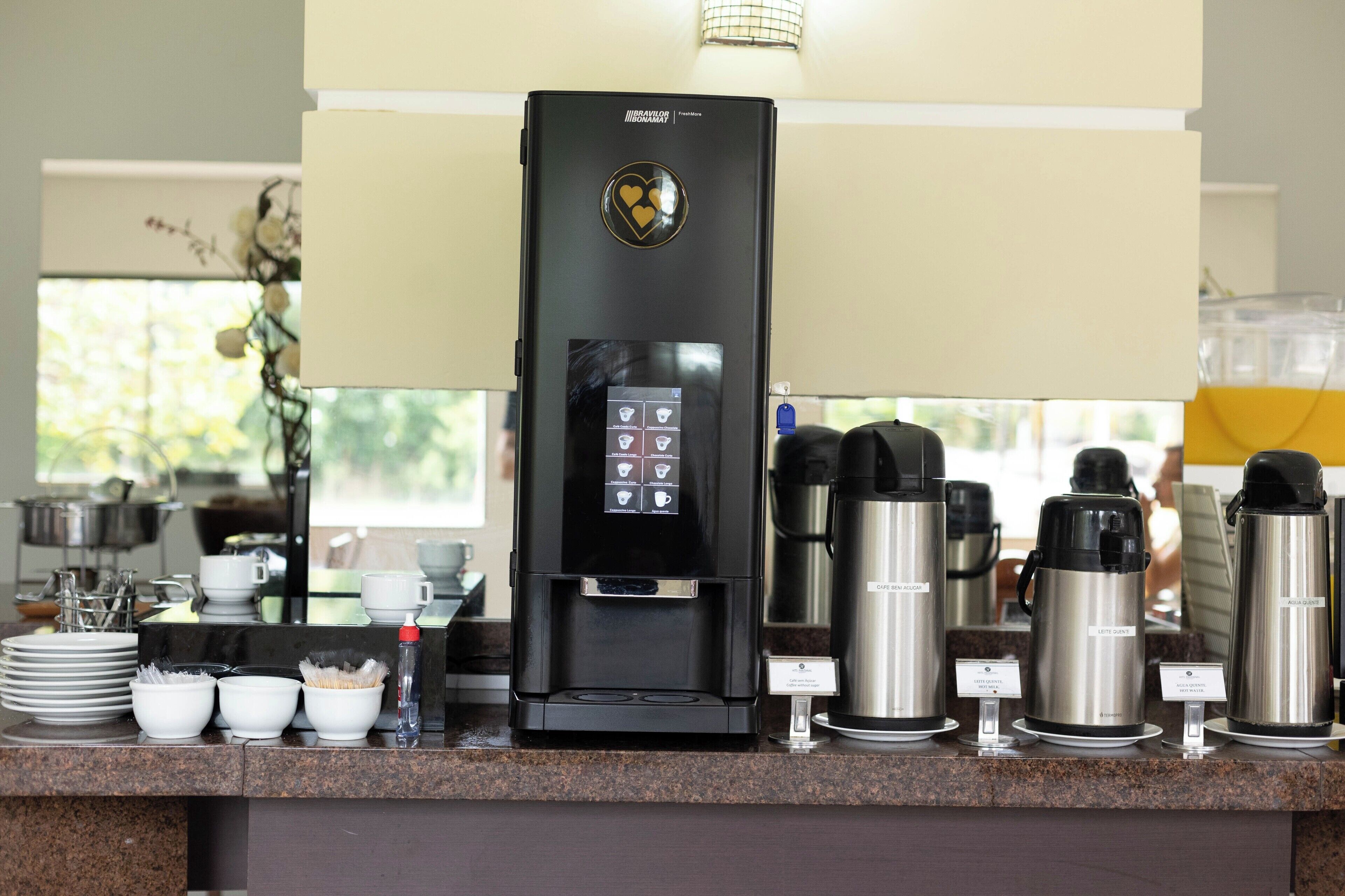 A coffee station with a coffee machine, multiple coffee makers, and various coffee cups and saucers.