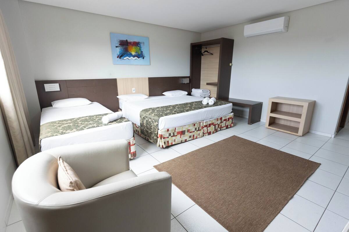 A hotel room with two beds, a sofa, a small table, and a wall-mounted air conditioner.