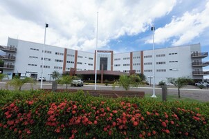 Un hotel moderno con entrada central, varios pisos y un estacionamiento al frente.