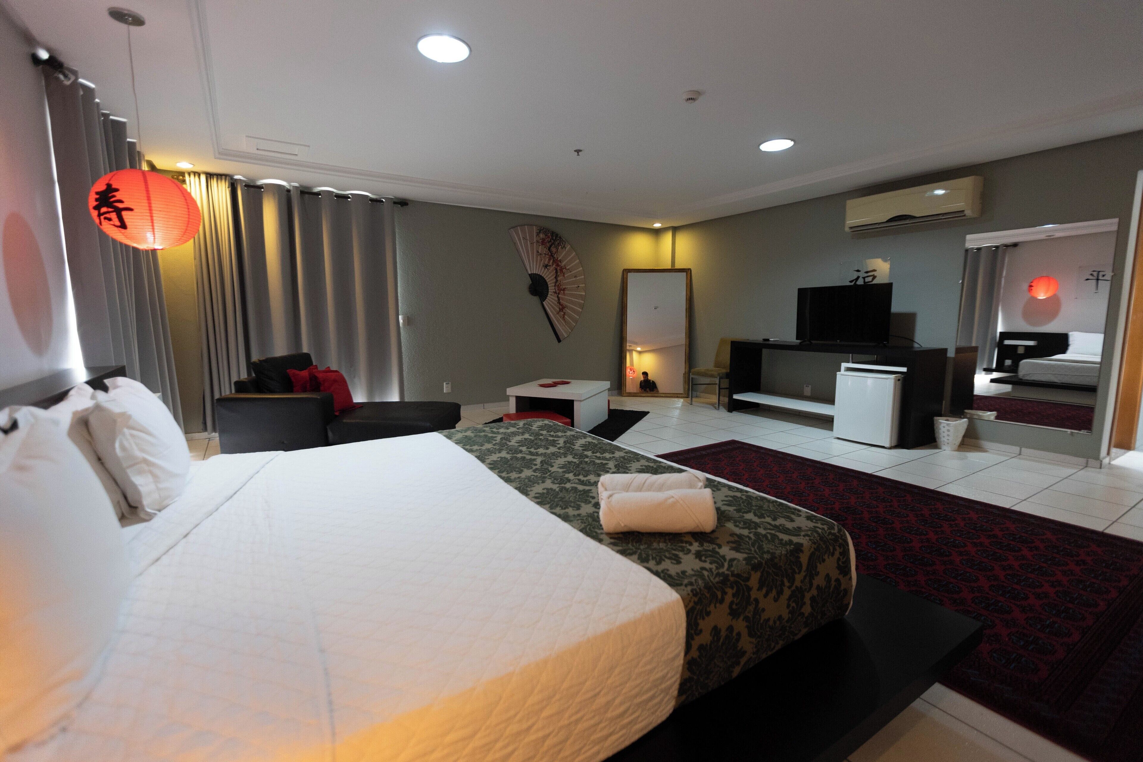 A hotel room with a large bed, a desk, a TV, and a mirror.