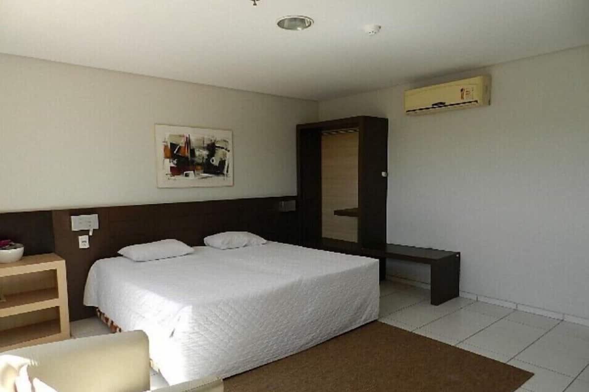 A hotel room with a bed, a desk, a chair, a wardrobe, and a painting on the wall.