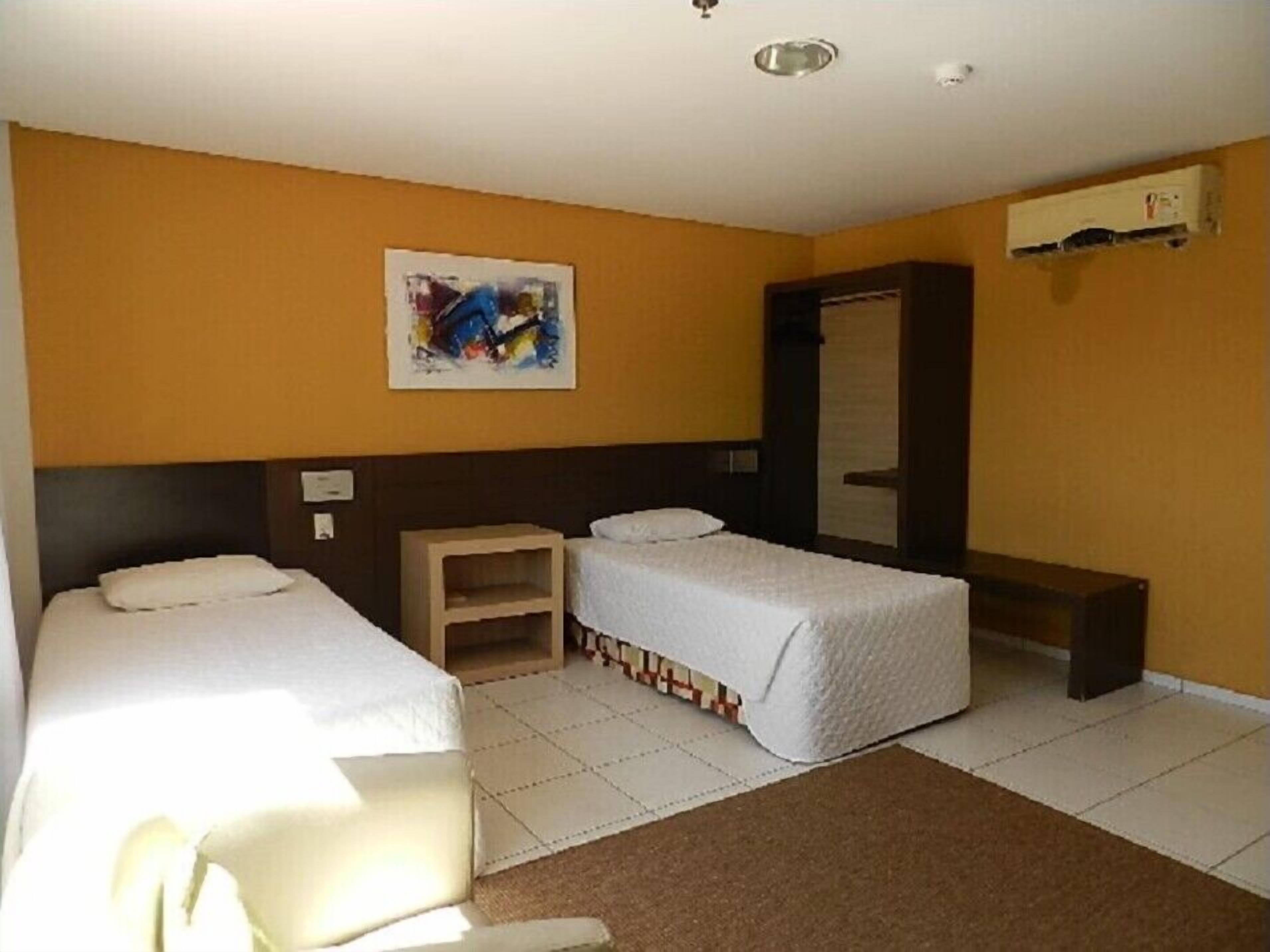 Hotellihuone, jossa on kaksi erillistä sänkyä, pieni puinen yöpöytä, peili ja taulu seinällä.