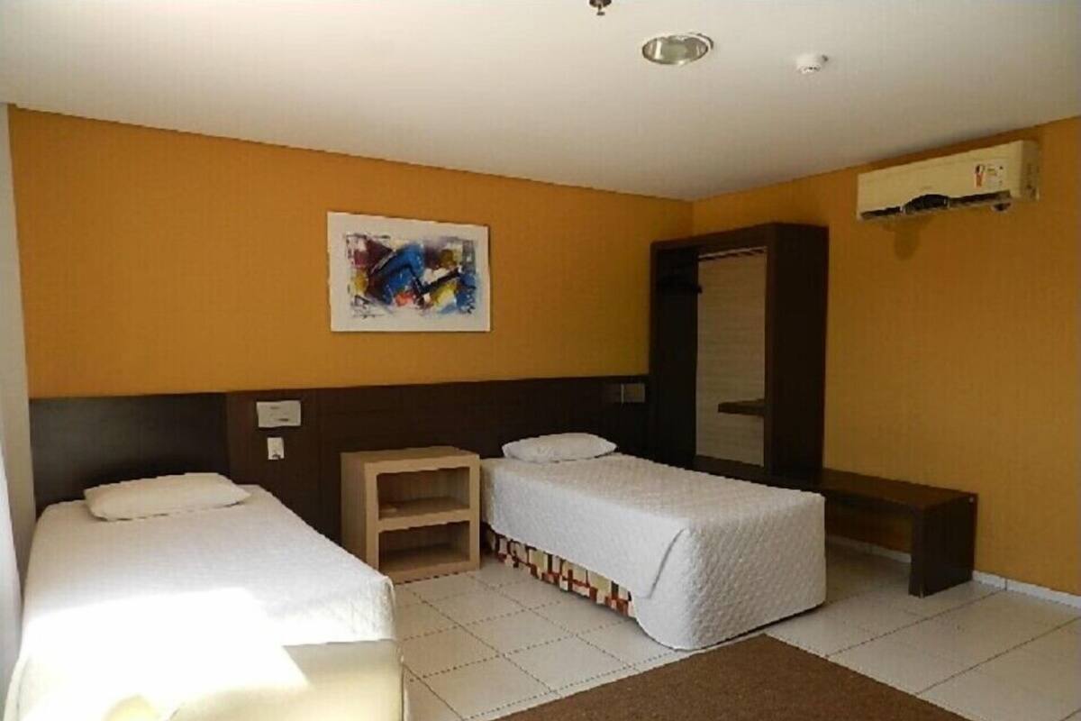 A hotel room with two single beds, a small wooden nightstand, a mirror, and a painting on the wall.