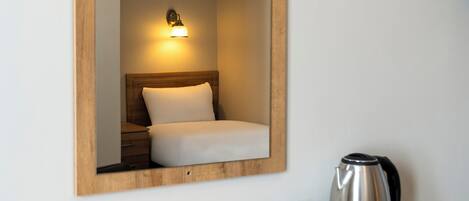 A hotel room with a wooden headboard, a bedside lamp, a bed, a nightstand, a coffee maker, and a cup of coffee on a tray.