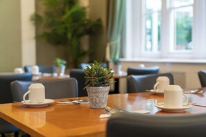 Een eethoek met een tafel gedekt voor twee personen, inclusief een potplant, een witte kop en een schotel.