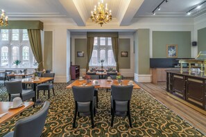 Une salle à manger d’hôtel avec une grande table, des chaises, un lustre et un sol recouvert de moquette.