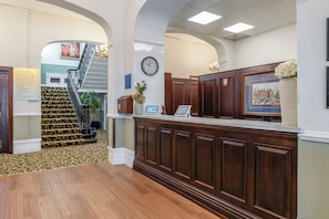Un espace d’accueil avec un comptoir de réception en bois, une horloge au mur et un escalier menant à d’autres pièces.