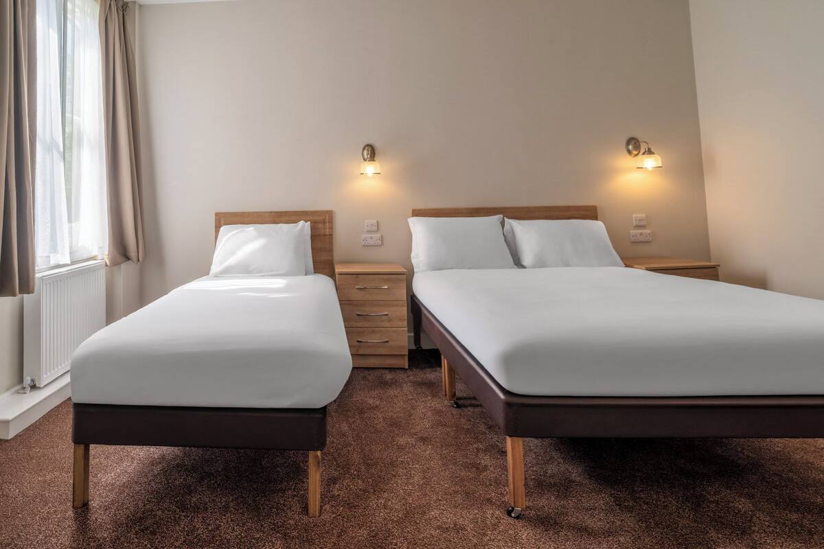 Ein Hotelzimmer mit zwei Einzelbetten, einem Holfnachtkästchen, einem Schminktisch und zwei Wandleuchten.