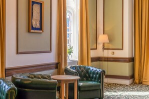 Une pièce avec un canapé en cuir vert, une petite table ronde, une lampe et un document encadré accroché au mur.