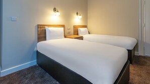 Een hotelkamer met twee bedden, houten hoofdeinden, nachtkastjes en wandlampen.